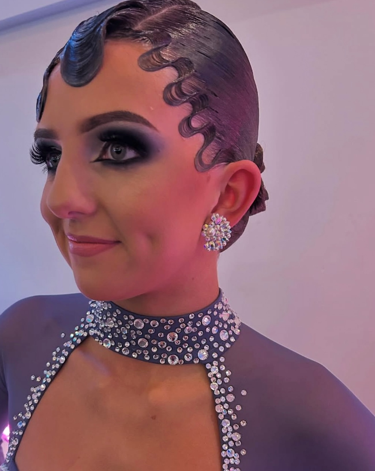 Ballroom dancer with styled hair and decorative makeup, wearing a rhinestone costume and earrings.